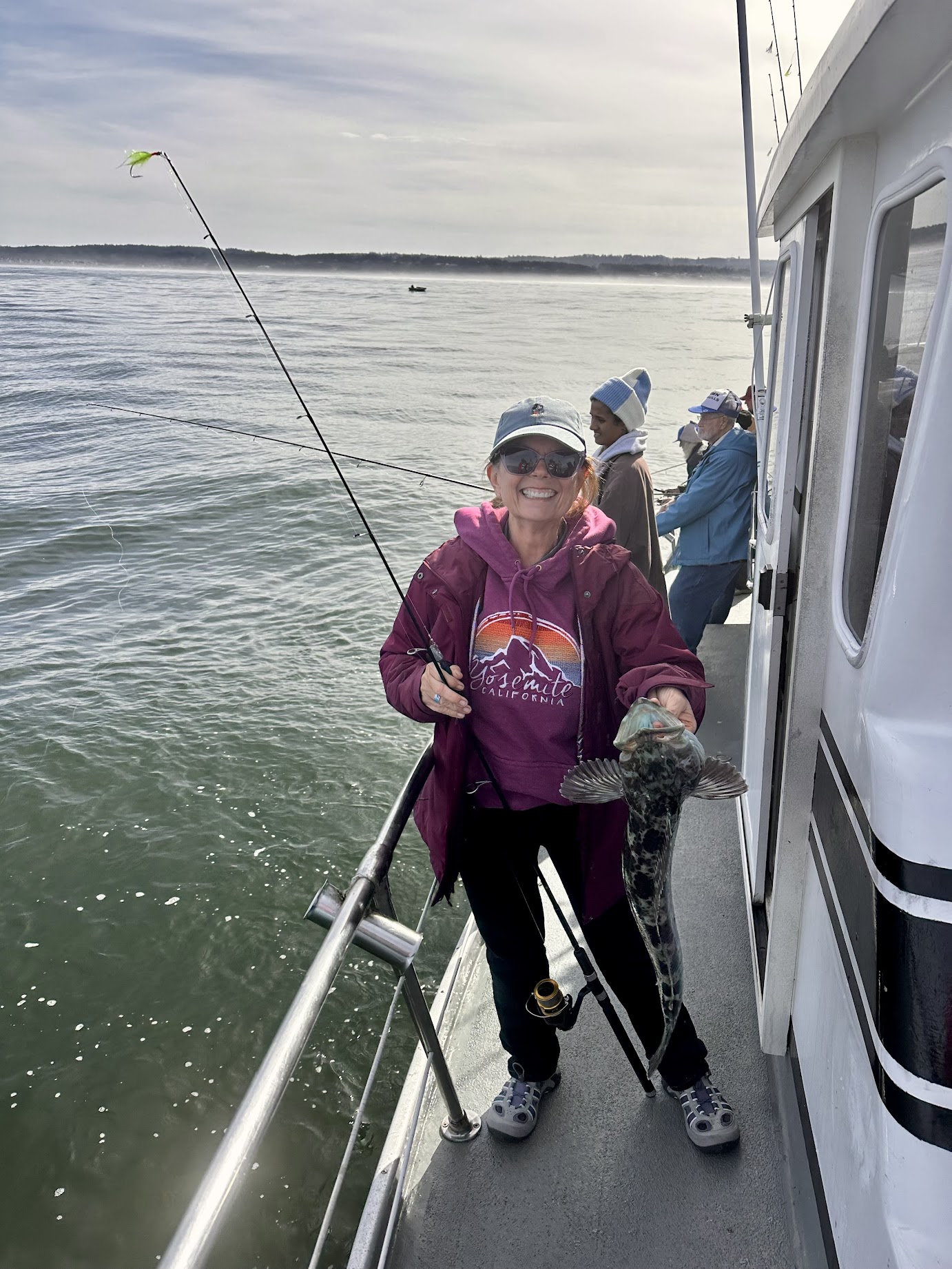 woman on a fishing charter boat holding a rod and reel and the lingcod she just caught